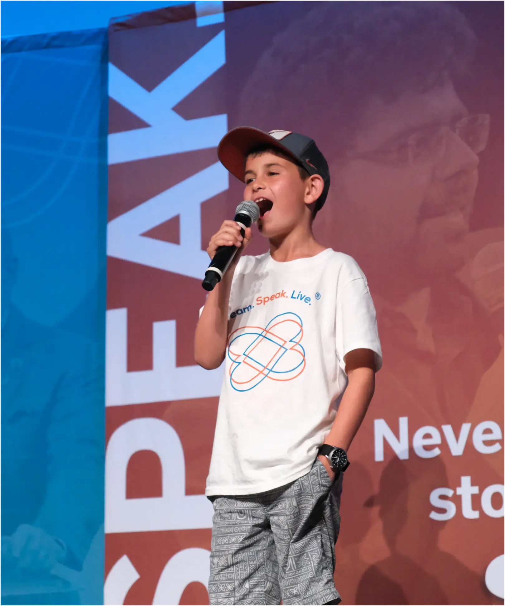 young  man stands with a microphone and other hand in pocket