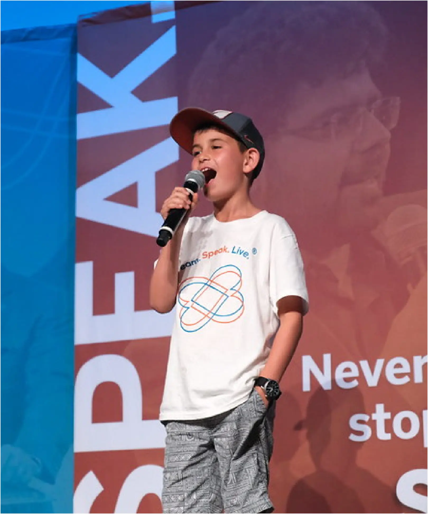 Boy speaks into microphone with hand in pocket